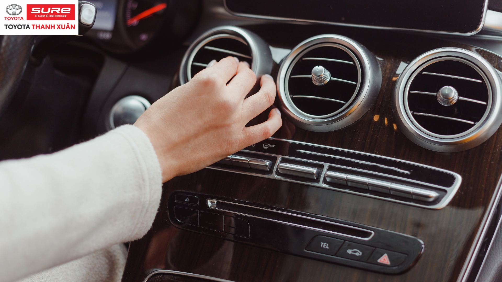 Người chỉnh quạt gió ô tô màu bạc trên bảng điều khiển màu nâu gỗ bóng. Logo Toyota Sure Thanh Xuân ở góc trên bên trái.